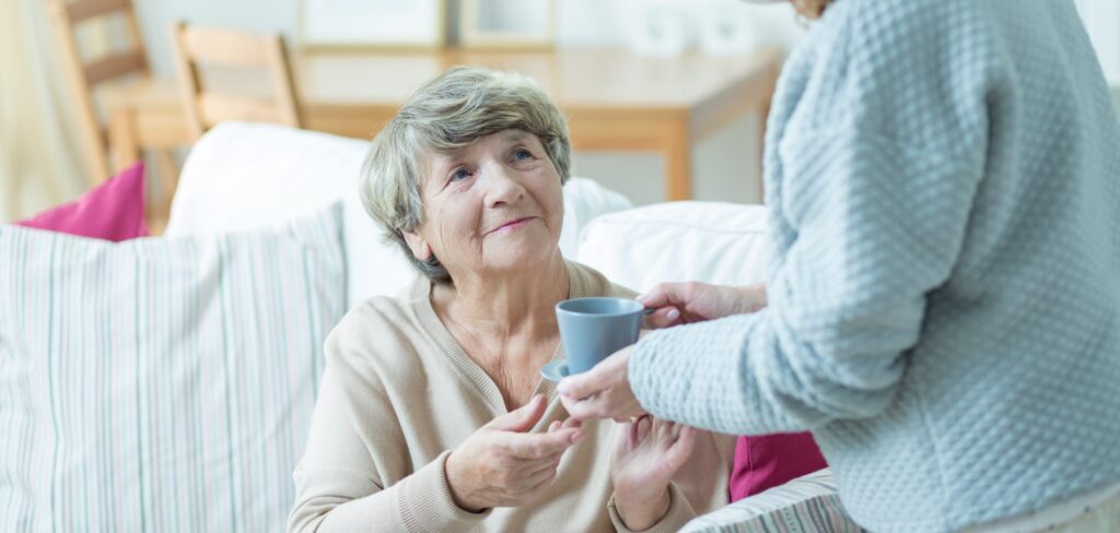 caregiver daughter giving a cup of tea to her mum